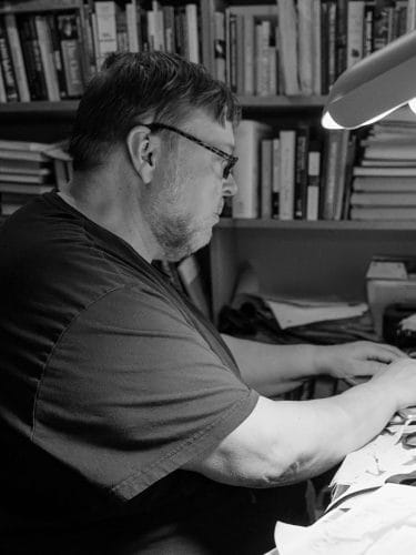 Silmälasipäinen henkilö kirjoittaa työpöydän ääressä.